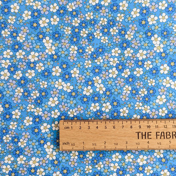 Rainbow Garden fabric: Small white, blue, and purple flowers on a light blue background with ruler for scale.