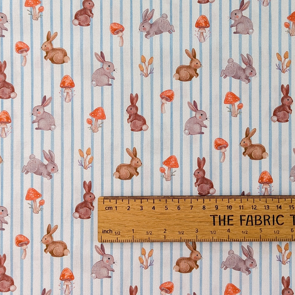 Bunnies and toadstools on ticking stripe background, 100% cotton fabric.  The ruler shows the scale of print.