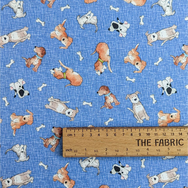 Fabric featuring cartoon-style dogs in various poses and scattered white bones on a textured blue background with ruler for scale.