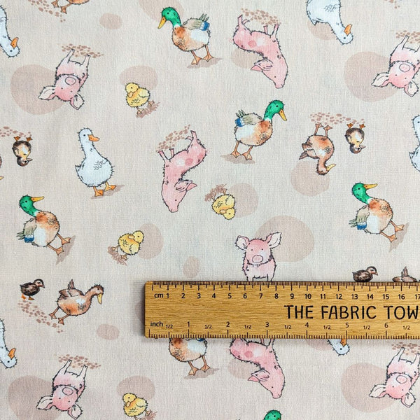 Close-up of a fabric featuring cartoon-style pigs, ducks, and geese scattered on a light beige background with subtle speckles with ruler for scale.
