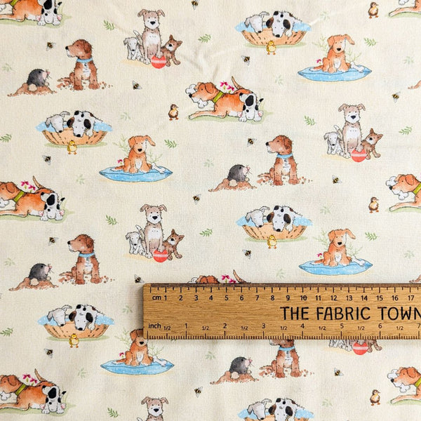 Light cream fabric featuring a print of different cartoon-style dogs with bees and paw prints scattered throughout with ruler for scale.