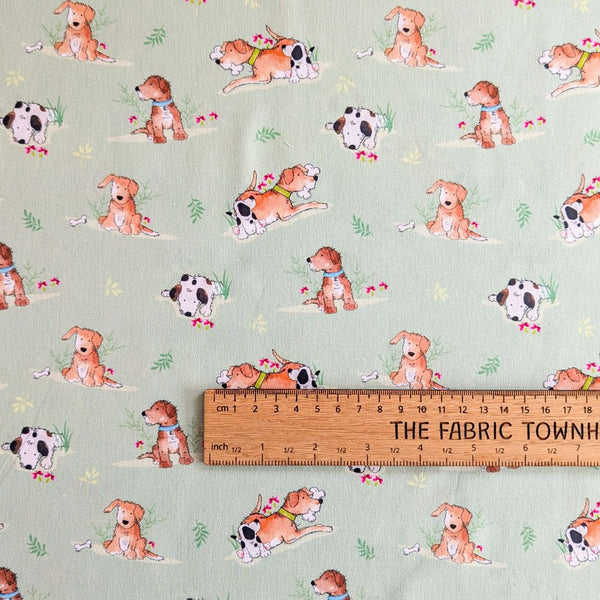 Cartoon-style dogs in various poses, scattered with bones and leafy green plants on a light green background with a ruler for scale.