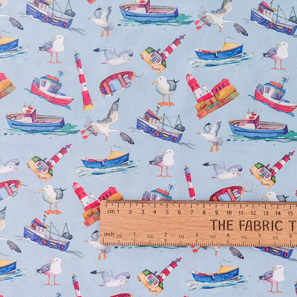 A repeating nautical pattern featuring illustrated seagulls, fishing boats, and lighthouses on a pale blue background.  The ruler shows the scale of print.
