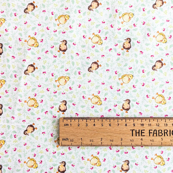 Non-directional fabric with baby chicks on a cream background with purple flowers and cream foliage with a ruler for scale.