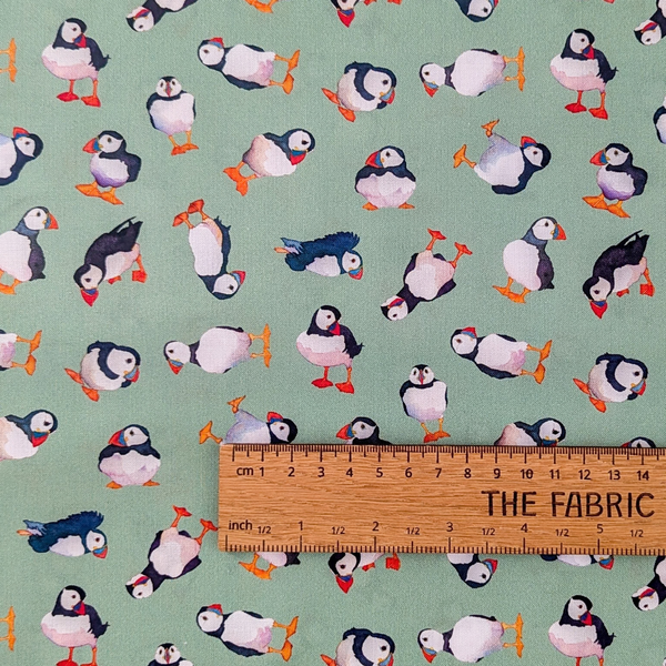 A repeating pattern of illustrated puffins on a light sage green background designed by Emma Ball.  The ruler shows the scale of print.
