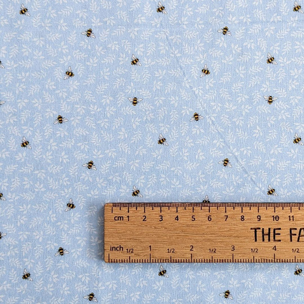 Small bees and delicate white foliage scattered across a soft, light blue background with ruler for scale.