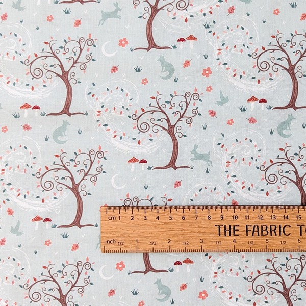 A repeating whimsical forest pattern on a pale mint green background, featuring brown trees with swirling white leafy branches, mushrooms, birds, rabbits, flowers, and crescent moons.  The ruler shows the scale of print.